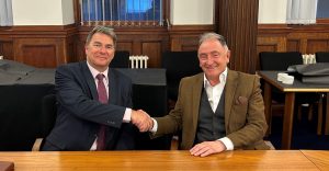 Photo of NHS 24 Chief Executive Jim Miller and University of Strathclyde's Principal and Vice-Chancellor Professor Sir Jim McDonald. They are both sitting at board room table shaking hands and smiling to the camera. 