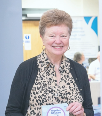 Photo of Anne smiling to the camera. She is holding an NHS 24 leaflet.