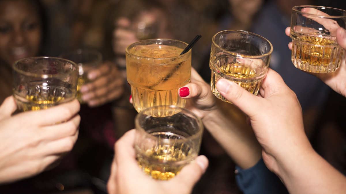 Image of five hands holding up with drink glasses as part of a cheers.